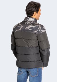 Pufferjacke mit grauem Camouflage-Oberteil, schwarzem Unterteil und horizontalem Steppmuster. Verfügt über einen hohen Kragen und eine glatte Textur.