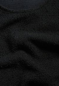 Svart tyg med en texturerad yta, som har ett lätt upphöjt mönster. Materialet verkar mjukt och något elastiskt.