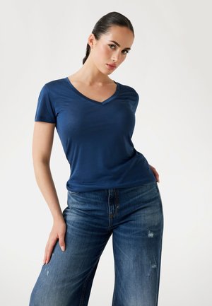 Marineblauw V-hals T-shirt van gladde stof, gecombineerd met versleten lichtblauwe wijde jeans, wat een casual silhouet laat zien.