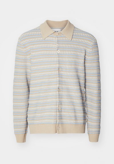 Sweter z dzianiny z beżowym kołnierzem i zapięciem na guziki. Posiada poziome paski w odcieniach beżu i jasnoniebieskim. Ściągacze przy mankietach i u dołu.