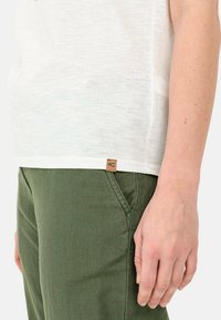 Witte korteblouseshirt met een gestructureerde afwerking, gecombineerd met olijfgroene broek. Opvallend leren label met een embleem aan de onderkant van het shirt.