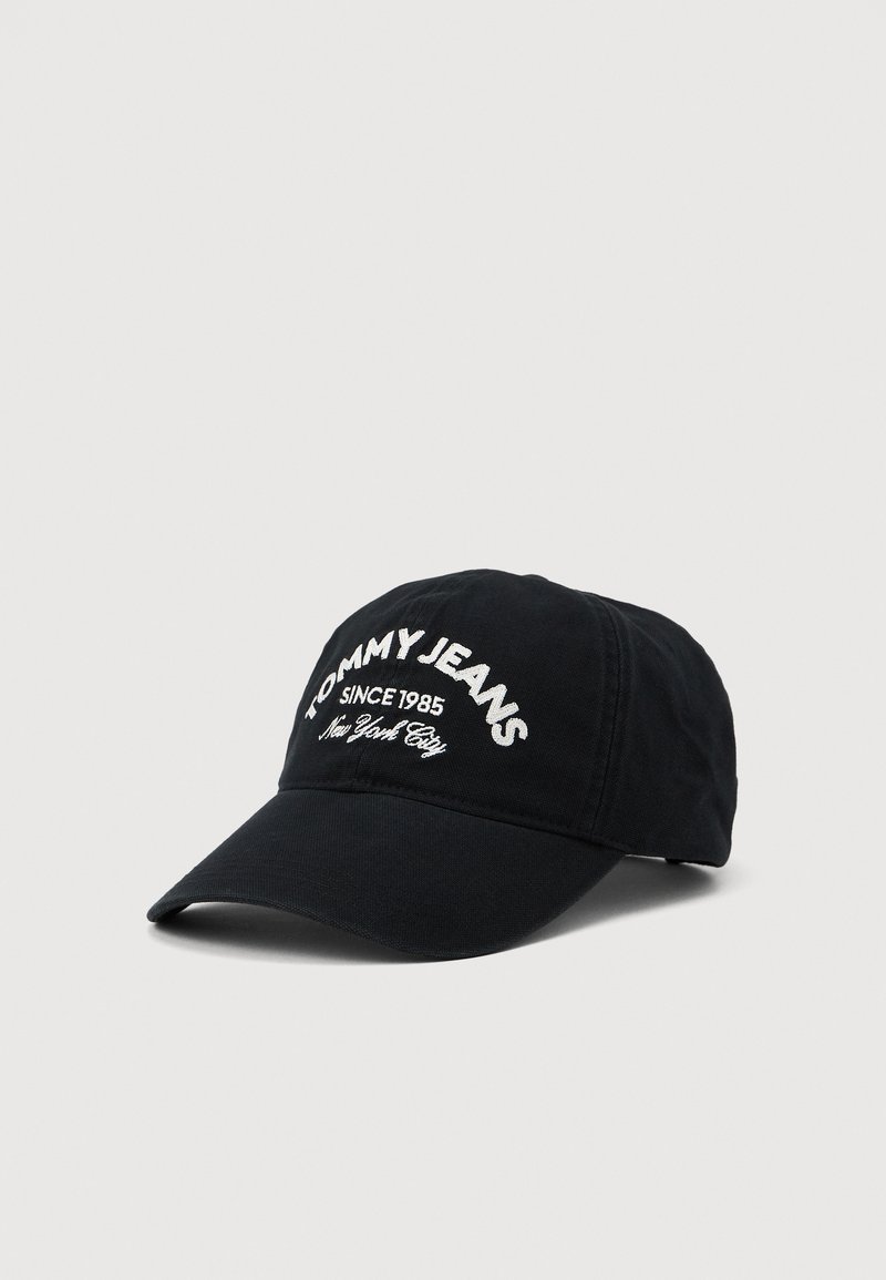 Svart baseball cap med buet brem som har hvit brodert tekst "TOMMY JEANS SINCE 1985 New York City" på frontpanelet.