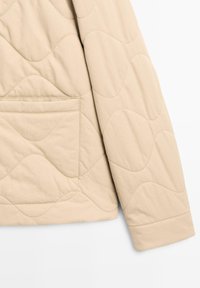Beżowa pikowana kurtka z wzorem fal, z jednolitym rękawem, przednią kieszenią i gładką fakturą.
