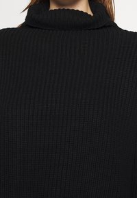 Czarny sweter z wysokim kołnierzem, wykonany z żeberkowej tkaniny, z teksturowanym wykończeniem. Krój jest oversize i wygodny.