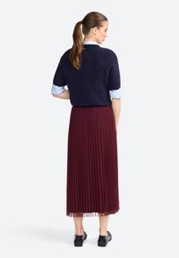 Navy knitted short-sleeve sweater paired with a pleated burgundy skirt, featuring a sheer hem, and black flat shoes. Back view.