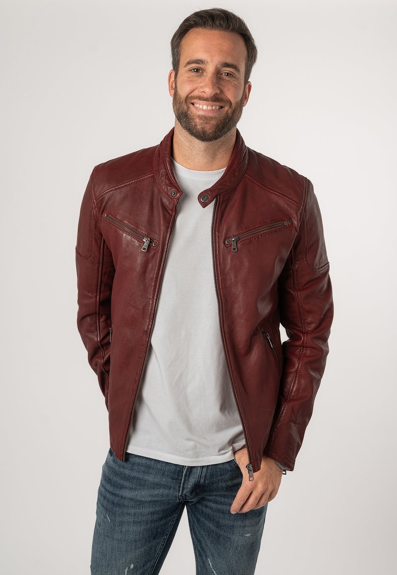 Burgunderrote Lederjacke mit hohem Kragen, zwei Reißverschlusstaschen auf der Brust und schlanker Passform, kombiniert mit einem grauen T-Shirt und blauen Jeans.