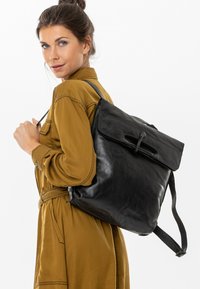 Zaino in pelle nera con chiusura a roll-top e spallacci regolabili, caratterizzato da una texture liscia e un design elegante. Accentuato da un gancio sicuro.