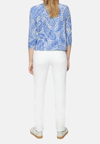Blauw patroon top met driekwart mouwen, gecombineerd met witte broeken. Gestyled met casual, lichte schoenen. Achteraanzicht zichtbaar.
