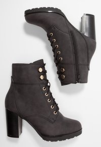 Botas de tobillo de cuero sintético negro con un tacón alto y robusto, cordones en la parte delantera, detalles en metal dorado y cremallera lateral.