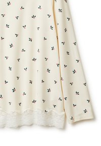 Kremowa bluzka z długim rękawem, ozdobiona nadrukiem ostrokrzewu w kolorze zielonym i czerwonym, z teksturowanym koronkowym wykończeniem u dołu oraz luźnym krojem.