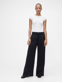 Pantalon noir à jambes larges avec une texture lisse et des poches avant, associé à un t-shirt blanc côtelé ajusté, mettant en avant un design minimaliste.