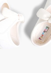 Weiße Canvas-Schuhe mit einem Schleifendetail am Riemen. Weiche Innenausstattung und ein bunter Aufkleber im Inneren. Runde und glatte Form.