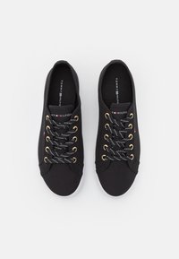 Une paire de baskets noires Tommy Hilfiger avec des semelles blanches, des lacets noirs et blancs enfilés à travers des œillets dorés, vue de dessus.