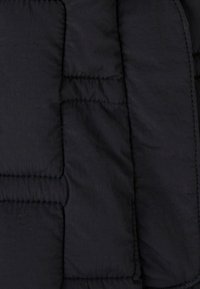 Gewatteerde zwarte pufferjasstof met een gladde textuur, voorzien van gestikte secties en gemaakt van een lichtgewicht, duurzaam materiaal.