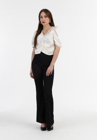 Bluză albă din saten cu mâneci puff, cu față strânsă, asociată cu pantaloni evazați negri și tocuri negre. Textură netedă, design modern.