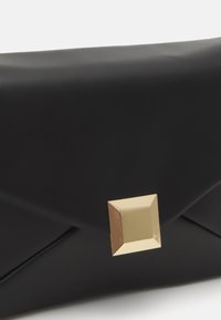Czarna kopertówka wykonana z gładkiego materiału syntetycznego, z wyraźnym złotym kwadratowym zapięciem i złożonym designem. Minimalistyczny i elegancki wygląd.