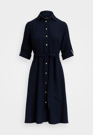 Abito blu navy con scollatura a colletto, chiusura frontale con bottoni e maniche arrotolate. Include una cintura coordinata e presenta bottoni in tono oro.