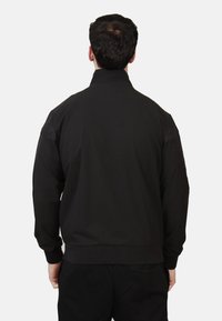 Giubbotto bomber nero con colletto alto, polsini a coste e dettagli trapuntati sulle spalle. Presenta una texture liscia e opaca e un design aerodinamico.