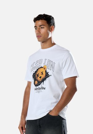Mann trägt ein weißes T-Shirt mit einer Grafik eines Bären mit durchgestrichenen Augen in einem zerrissenen Design und Text mit der Aufschrift "worldwide."