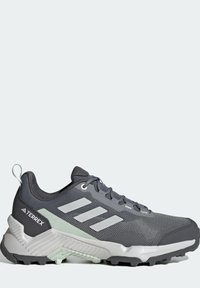Chaussure de sport grise avec dessus en mesh et synthétique. Présente trois bandes blanches, un col rembourré et une semelle extérieure noire robuste. Accentuée de vert clair.