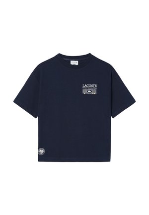 Camiseta Lacoste de manga corta en azul marino con el texto "Lacoste Roland Garros Club" y el logo en el pecho, y el logo redondo de Roland Garros cerca del dobladillo.