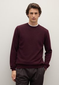 Maglione color bordeaux con scollo rotondo, realizzato in materiale morbido, con maniche lunghe e orlo a coste, abbinato a pantaloni marrone scuro.