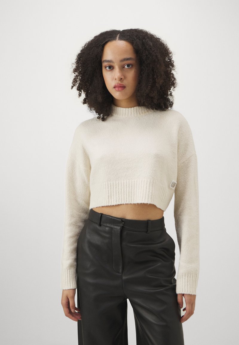 Cropped, cream sweater in soft texture with a ribbed hem and cuffs. Paired with high-waisted black leather pants, creating a contrasting look.