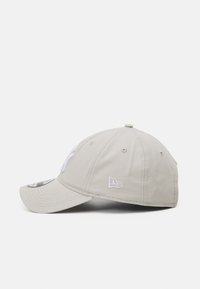 Beige baseball cap with a curved brim, embroidered logo in white, structured crown, and eyelets for ventilation. Classic design.