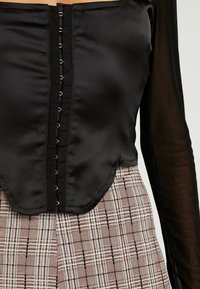 Černý saténový top s knoflíkovým zapínáním, s průsvitným dlouhým rukávem. Pod ním vzorovaná kostkovaná látka v béžových, hnědých a šedých tónech.