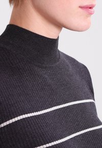 Pull en maille côtelée noir avec des rayures horizontales blanches. Gros plan montrant la texture douce et le design du col ajusté.
