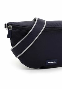 Borsa a tracolla in nylon blu navy con una tracolla grigia, chiusura con cerniera e un piccolo etichetta con logo. Texture liscia con forma arrotondata e design minimalista.
