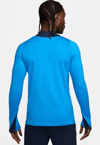 Maglietta sportiva a maniche lunghe di un vivace blu con dettagli blu navy nel colletto e nei polsini, realizzata in un tessuto morbido e elastico.