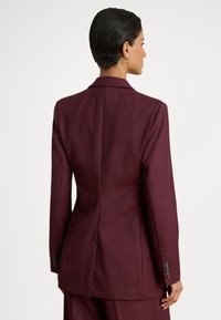 Μπορντό σακάκι με εφαρμοστή κοπή, γιακάδες με εγκοπές και διακοσμητικά κουμπιά στα μανίκια, με ομαλή υφή και δομημένη σιλουέτα.
