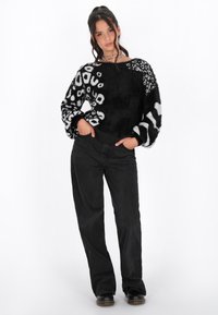 Maglione a maglia in bianco e nero con motivo a fantasia, texture variegate, maniche lunghe a sbuffo e una vestibilità rilassata, abbinato a pantaloni neri a gamba larga.