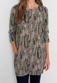 Långärmad tunika i svart med beige lövmönster, har rundad neckline och sidofickor, tillverkad av ett mjukt, strukturerat tyg.