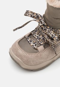 Béžové semišové a textilní boty s leopardími šňůrkami, kulatou špičkou a texturovanou gumovou podrážkou pro lepší přilnavost. Měkký kožešinový límec jako akcent.