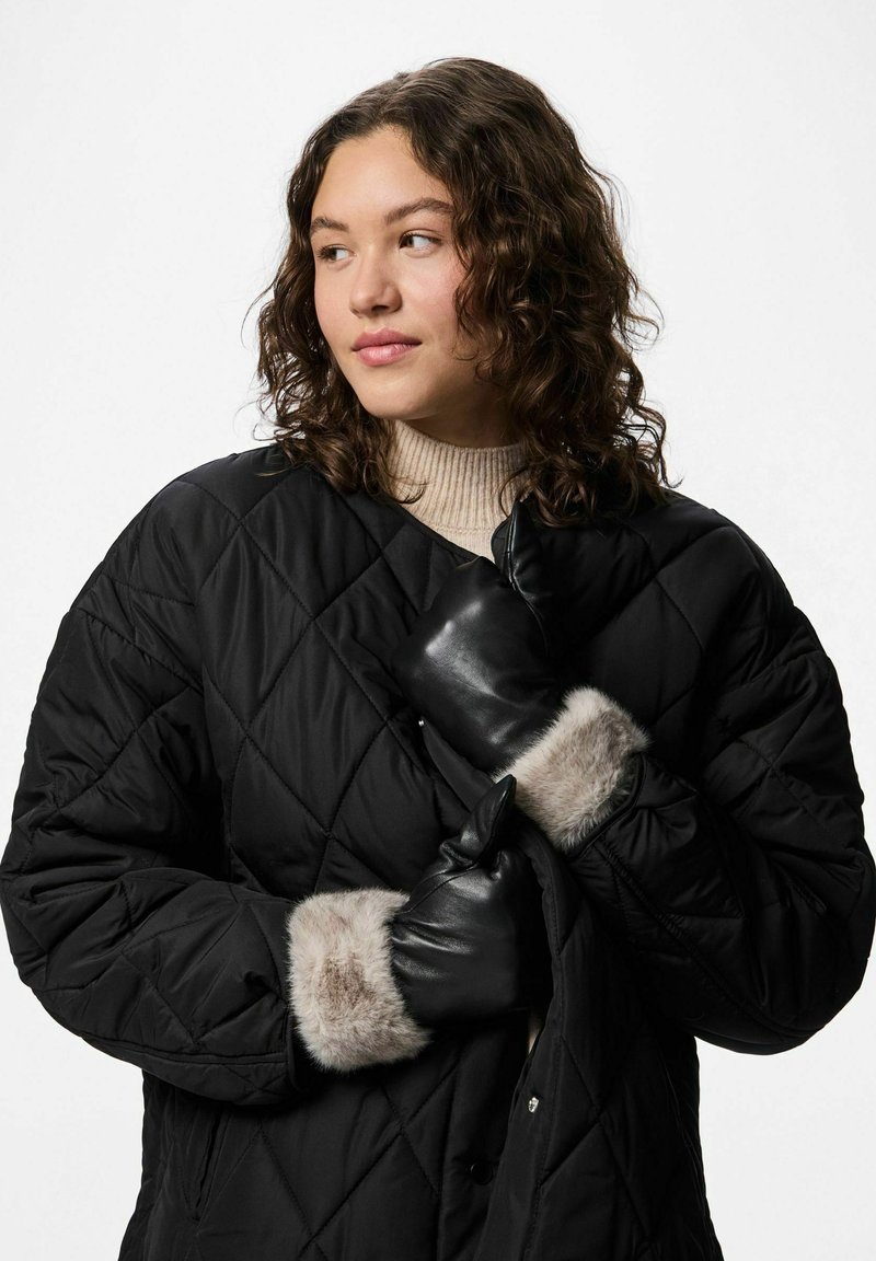 Juodas siuvinėtas pūkinis paltas su deimanto raštu, papuoštas kailiu aptrauktais rankogaliais ir juodos odos pirštinėmis. Po juo dėvimas pilkos spalvos džemperis.