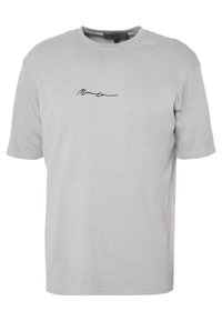 Světle šedé tričko s krátkým rukávem a kulatým výstřihem, s malým černým kurzívním logem uprostřed na hrudi.