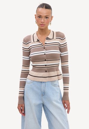 Femme portant un cardigan côtelé ajusté à manches longues avec des rayures horizontales beige, blanc et marron et un jean taille haute bleu clair.