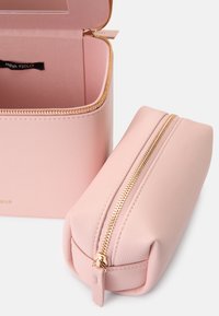 Neceser de piel rosa con cremalleras doradas, con forma rectangular y textura lisa. Incluye un pequeño bolso de almacenamiento a juego.