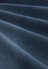 Denimová tkanina v tmavě modré barvě s mírně texturovaným povrchem, ukazující složené vrstvy a jemný diagonální vzor tkaní.