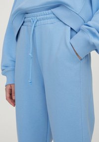 Jogging léger bleu en tissu doux, avec une taille élastique et un cordon de serrage, ainsi que des poches latérales. Texture lisse, coupe décontractée.