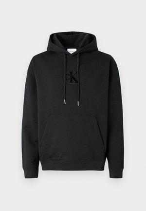 Zwarte katoenen hoodie met een voorvak, treksluiting aan de capuchon en een reliëf Calvin Klein-logo op de borst. Gladde textuur, geribbelde manchetten.