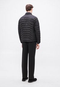 Fekete bélelt dzseki vízszintes steppelt mintával, hegyes gallérral és finom fényű felülettel. Fekete, bőszárú nadrággal és cipővel párosítva.