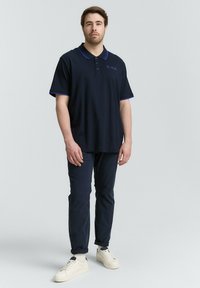 Navyblauwe polo met contrasterende paarse kraag en manchetten, gemaakt van katoen, gecombineerd met donkere slim-fit broeken en witte sneakers.