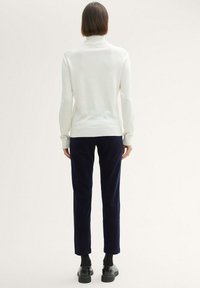 Witte geribde coltrui gecombineerd met marineblauwe corduroy broek. Soepele stof met fitted mouwen, taps toelopende broekspijpen en zwarte schoenen.