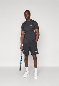 T-shirt de sport noir avec des panneaux texturés et un logo, associé à un short noir avec une bande latérale contrastante et des baskets blanches.