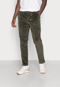 Olivgröna kordbyxor med slim fit, som har en liten dekorativ tofsdetalj och framfickor. Bärs med vita sneakers.