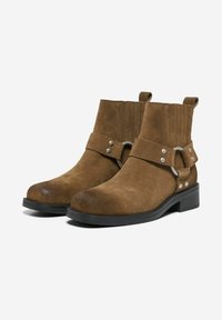 Bottines en daim marron avec un bout arrondi, une sangle décorative avec des accents métalliques et un dessus texturé. Talon bloc bas et attaches de tirage.