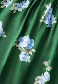 Tissu vert avec un motif de roses bleu clair et de feuilles vertes, délicatement froncé pour créer de douces ondulations.